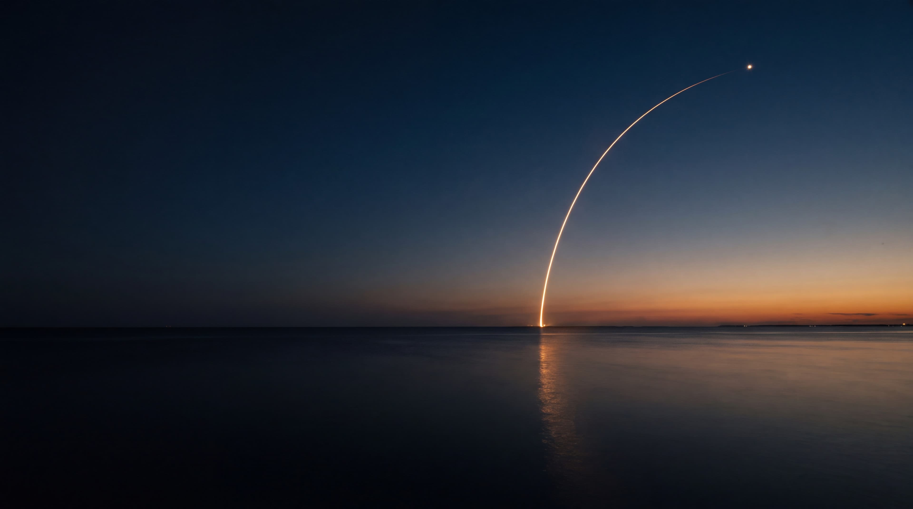 A rocket climbing over the sea at dusk